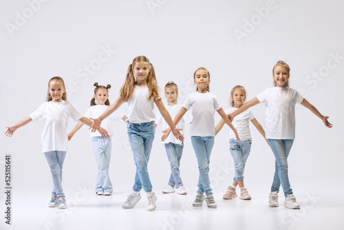 Dance group of happy, active little girls in jeans and t-shirts dancing isolated on white studio background. Concept of music, fashion, art, childhood, hobby