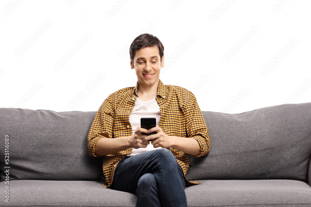 Young man sitting on a gray sofa and typing on a mobile phone Young man sitting on a gray sofa and typing on a mobile phone