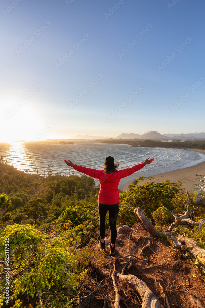 Obraz premium Adventurous Woman Hiker overlooking Sandy Beach on the West Coast of Pacific Ocean. Canadian Nature Landscape Background. Cox Bay Lookout, Tofino, Vancouver Island, BC, Canada.