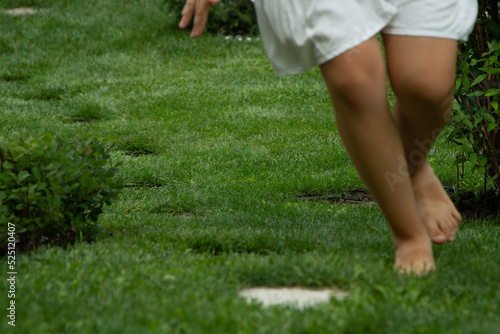 Girl running on the lawn at home in the garden, children's feet, focus on the grass