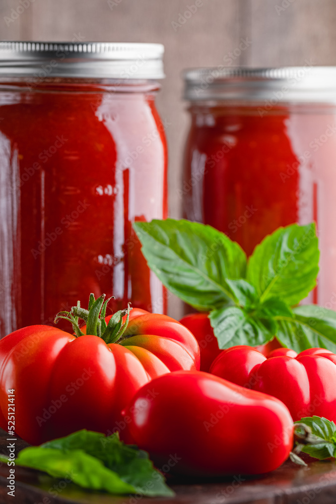 Fresh ripe, whole tomatoes, basil and home canned tomato sauce on a wooden cutting board Fresh ripe, whole tomatoes, basil and home canned tomato sauce on a wooden cutting board