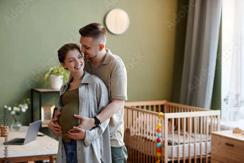 Konstfotografi Young man embracing his pregnant wife hile they standing in kids room at home