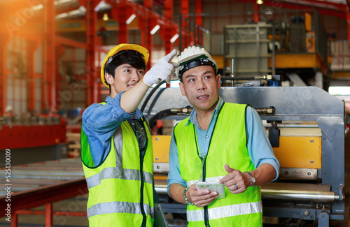 Two Asian male engineers use a tablet to discuss production plans and inspect production machines.