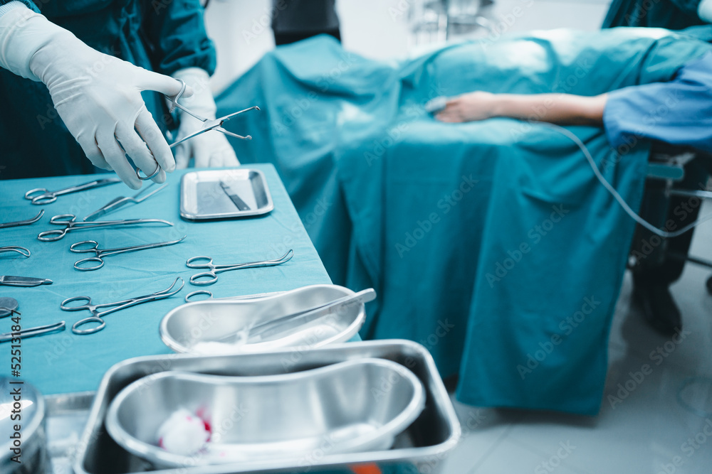 Fototapeta premium Close up surgeon doctor's hand with hygiene glove taking sterile surgical instrument tool, equipment in operating room patient in background for surgery. Hospital, medical healthcare emergency concept