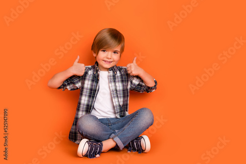 Full length photo of young boy sit floor show thumbs-up feedback select good isolated over orange color background