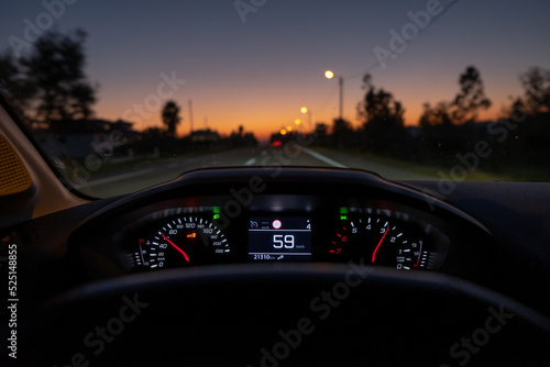 Driver view to the speedometer at 59 kmh or 59 mph, on a road blurred in motion, night fall view from inside a car of driver POV of the road landscape.