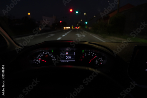 Driver view to the speedometer at 35 kmh or 35 mph, on road with traffic lights blurred in motion, night fall view from inside a car of driver POV of the road landscape.