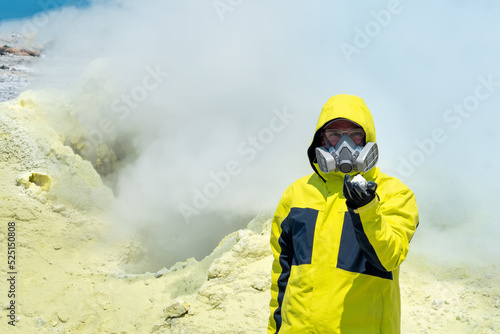 man volcanologist on the background of a smoking fumarole demonstrates a sample of a mineral photo