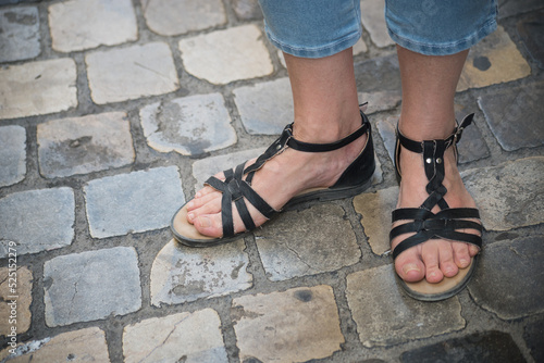 Closeup of black summer shoes on feet of woman standing on cobbles pavement texture in the street