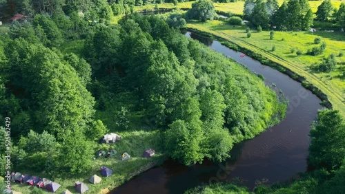 Aerial view of camping with kayaks on the beach of river on a sunny day. Nature background. Active rest concepts. Modern kayaks with paddles on beach near river. Summer camp activity.