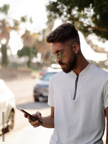 Hombre joven vistiendo gafas de sol usando su teléfono móvil en la calle durante sus vacaciones de verano