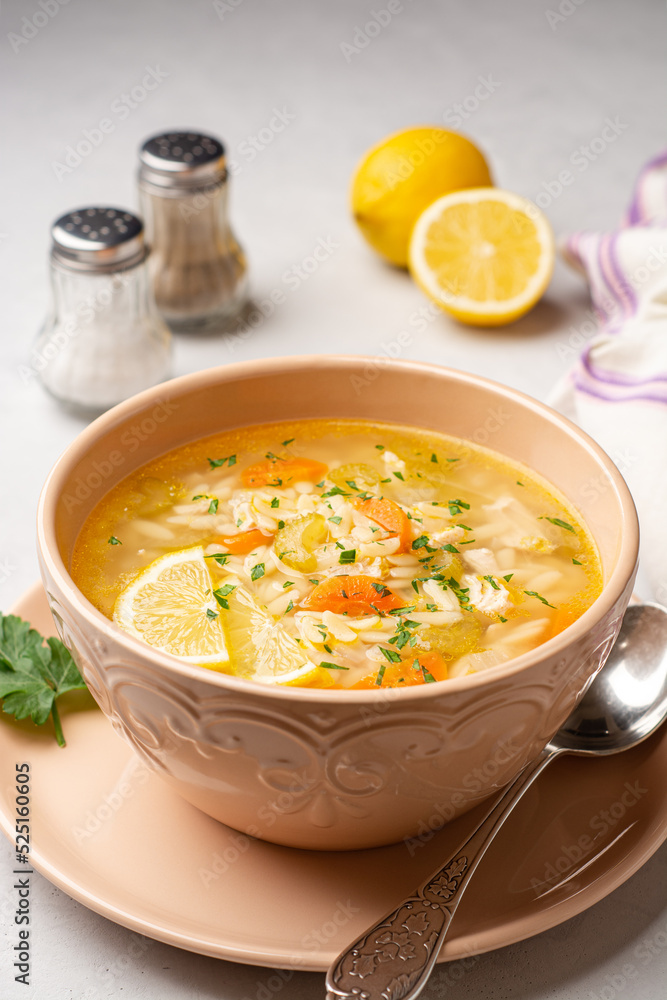 Italian lemon chicken orzo soup in bowl on concrete background