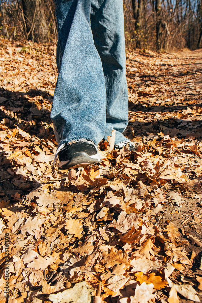 Leg of a girl in a sneaker and jeans, against the background of autumn yellow fallen leaves on the ground. Autumn season Leg of a girl in a sneaker and jeans, against the background of autumn yellow fallen leaves on the ground. Autumn season