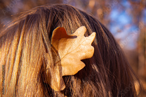 Autumn woman. Young woman with yellow autumn leaves in hair. Beautiful girl walking outdoors in autumn. Back view. No face