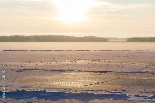 Sun shining above a frozen and snowy lake in Finland in the winter. Wintry  sunny and serene landscape at morning.