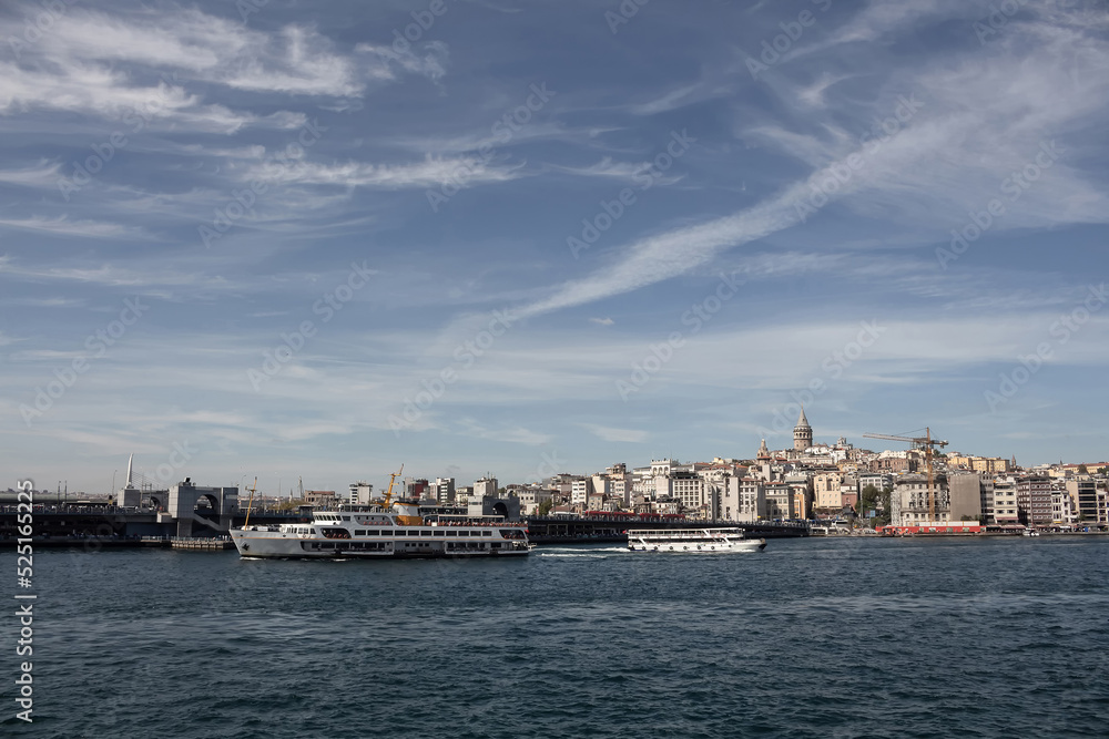 View of a traditional ferry boat and tour boat on Golden Horn part of Bosphorus in Istanbul. Galata tower and Beyoglu district are in the view. It is a sunny summer day.