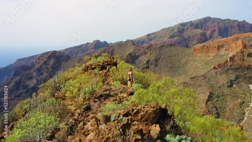 Woman enjoys nature landscape in hike to gorge. Aerial mountain peaks. Tenerife, Canaries, Spain. Trevelers dream. Hiking. Go everywhere. Real people. Travelling in a time of COVID. Orbit drone view. photo