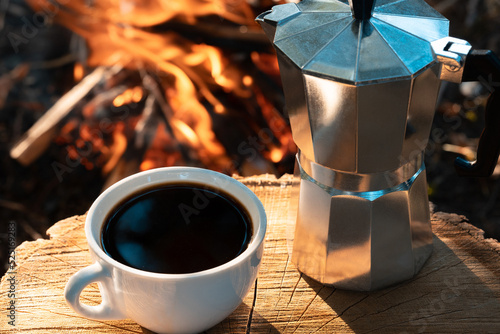 Camping coffee. Cup of coffee and a moka pot near to a campfire