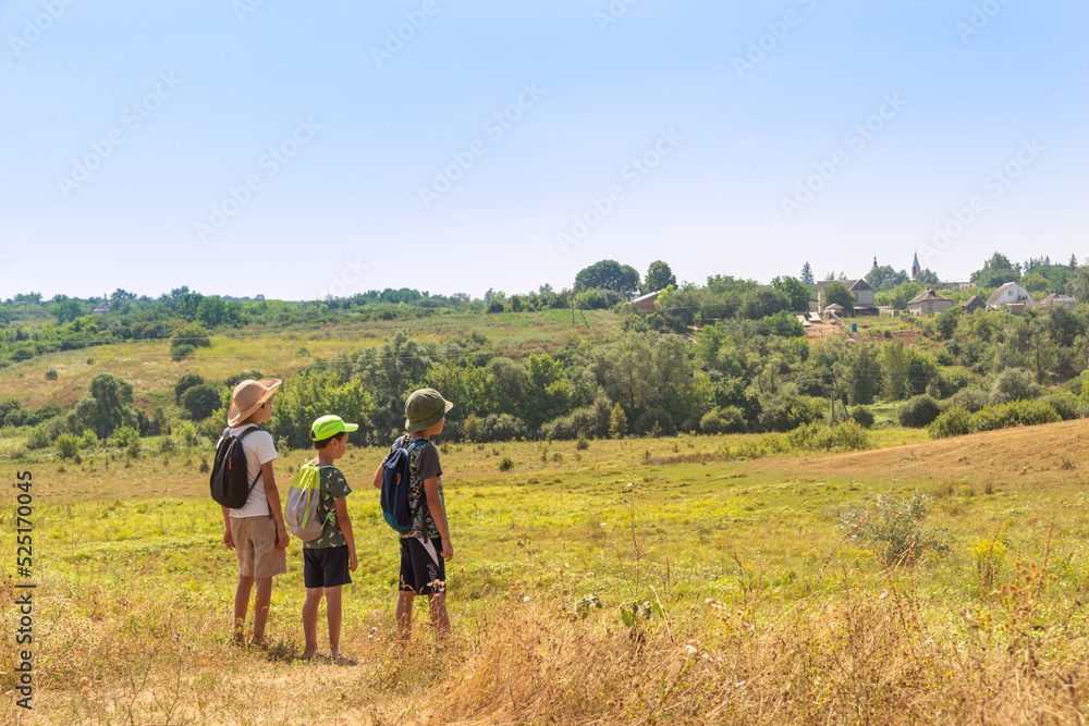 Three young boys with backpacks go hiking along the  field.