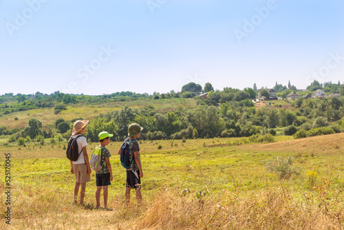 Three young boys with backpacks go hiking along the field.