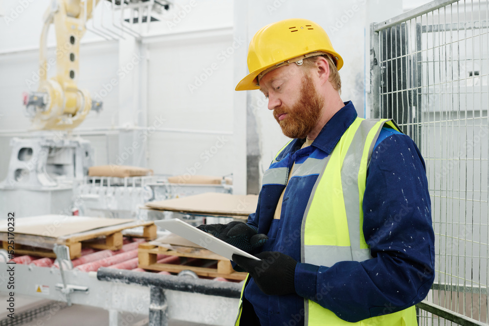 Young serious technician or foreman with tablet scrolling through technical data while searching for description of production process Young serious technician or foreman with tablet scrolling through technical data while searching for description of production process