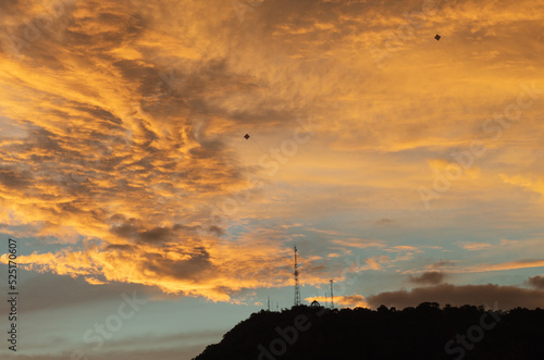 Dramatic sunset in the countryside, kites flying in the sky and silhouette of a tower on the mountains in the distance, Minas Gerais, Brazil