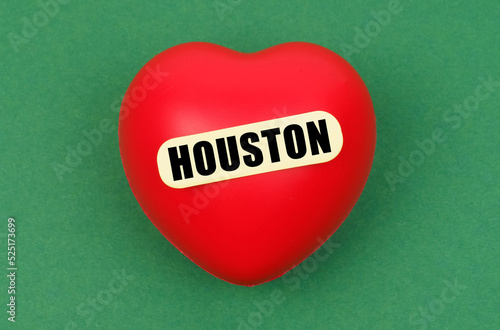 On a green surface lies a red heart with the inscription - Houston