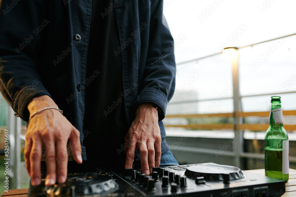 Hands of deejay in black shirt mixing sounds while standing in front of turntables and rotating one of them at rooftop party
