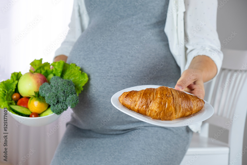 Belly of pregnant woman and plate with croissant and bowl of vegetables