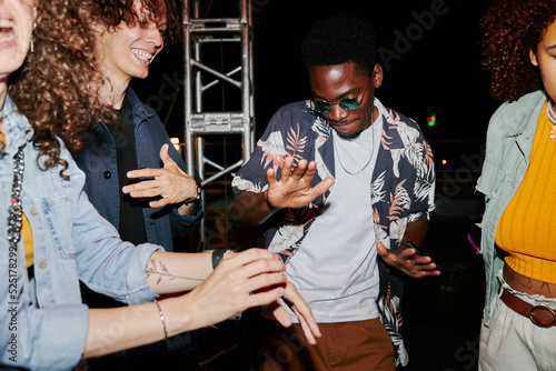 Young cheerful multicultural people in stylish casualwear enjoying dancing on rooftop at night while having party photo