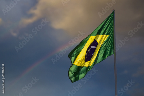 A bandeira do Brasil. Bandeira do Brasil voando, tremulando ao vento e com o céu e arco-íris ao fundo. photo