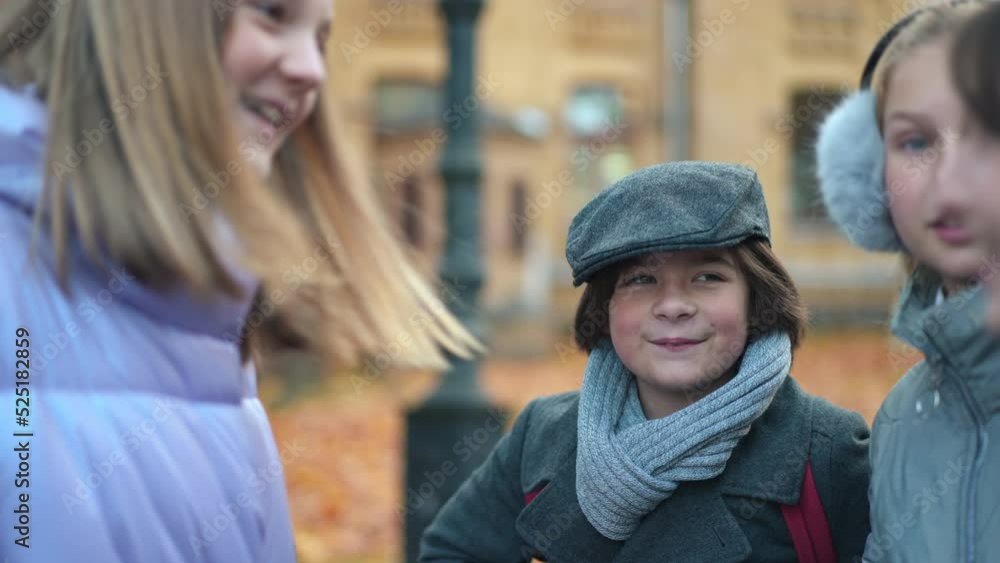 Curios schoolboy smiling talking with schoolgirls standing on college yard on autumn day. Portrait of Caucasian boy enjoying leisure with girls outdoors. Studying and friendship Curios schoolboy smiling talking with schoolgirls standing on college yard on autumn day. Portrait of Caucasian boy enjoying leisure with girls outdoors. Studying and friendship