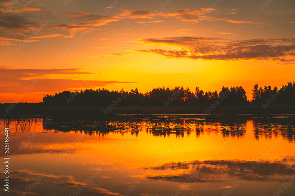 Bright orange sunset over lake, golden clouds and silhouette forest reflect in the water. Amazing nature background texture