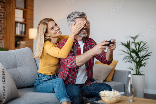 Cheerful mature caucasian lady closes eyes to man with joystick, interferes with online game in free time photo