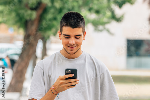 smiling young man on the street looking at mobile phone or smartphone