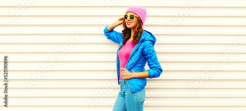 Portrait of stylish happy smiling young woman wearing colorful pink hat, blue jacket on white background