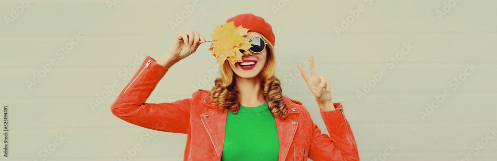 Autumn portrait of happy smiling young woman with yellow maple leaves wearing red french beret on gray background Autumn portrait of happy smiling young woman with yellow maple leaves wearing red french beret on gray background