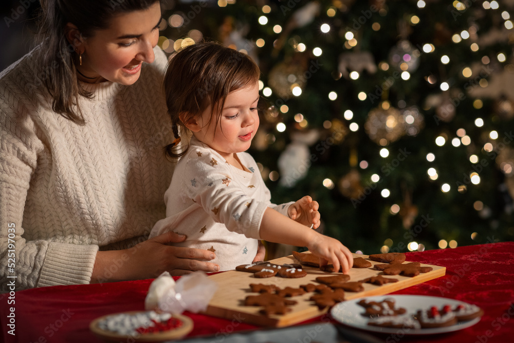 family, cooking and winter holidays concept - happy mother and baby daughter with icing in baking bag decorating gingerbread cookies at home on christmas family, cooking and winter holidays concept - happy mother and baby daughter with icing in baking bag decorating gingerbread cookies at home on christmas