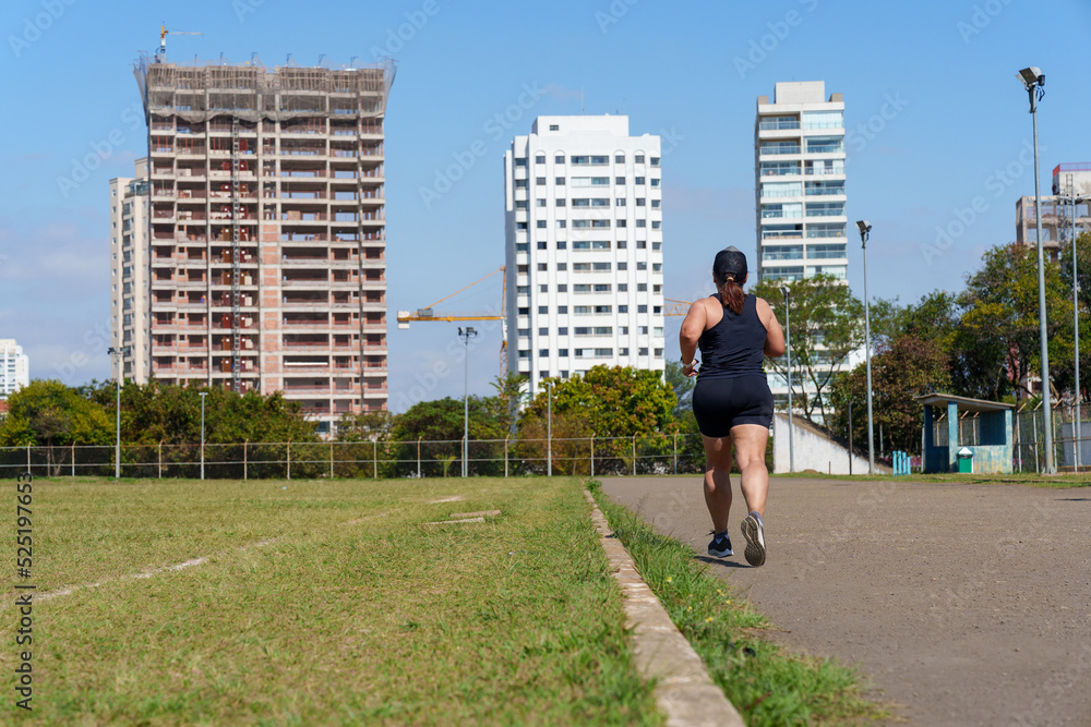 Woman running beside the city football field. Street race. Amateur sport concept.