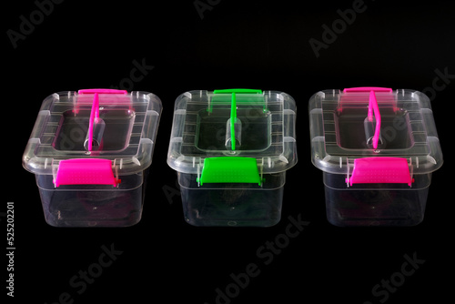 Three multi-colored transparent plastic containers with lids on a black background. Pink and light green neon colors. Copy space. photo