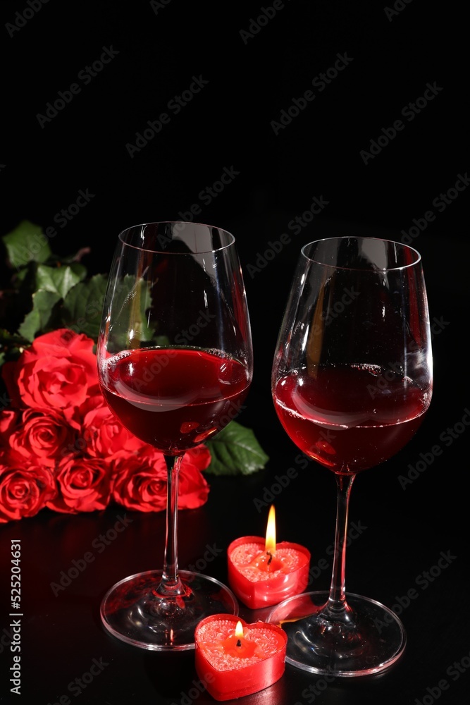Glasses of wine, roses and heart shaped candles for romantic dinner on black table Glasses of wine, roses and heart shaped candles for romantic dinner on black table