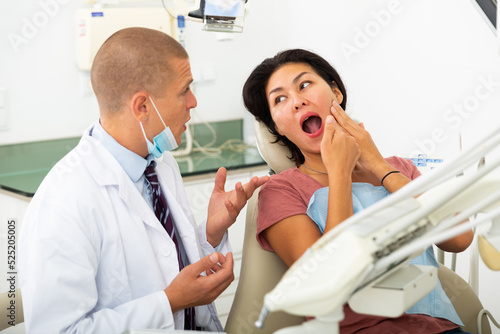 Woman patient sitting in a dental chair tells the dentist about her problem, showing which side she has a toothache