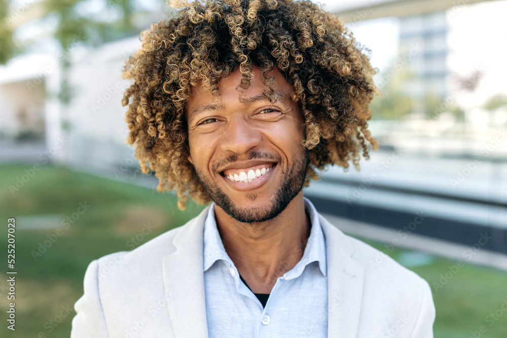 © Kateryna - Close-up portrait of a happy charismatic confident curly haired brazilian or hispanic male, successful entrepreneur, business man, standing outdoors, looking at the camera, smiling friendly © Kateryna - Close-up portrait of a happy charismatic confident curly haired brazilian or hispanic male, successful entrepreneur, business man, standing outdoors, looking at the camera, smiling friendly