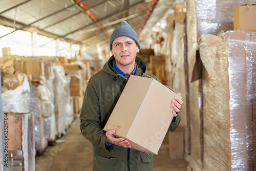 Caucasian man worker holding cardboard box while standing in storehouse.