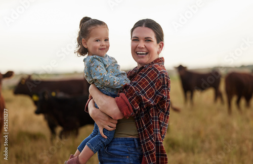 Family, mother and baby on a farm with cows in the background eating grass, sustainability and agriculture. Happy organic dairy farmer mom with her girl and cattle herd outside in sustainable nature photo