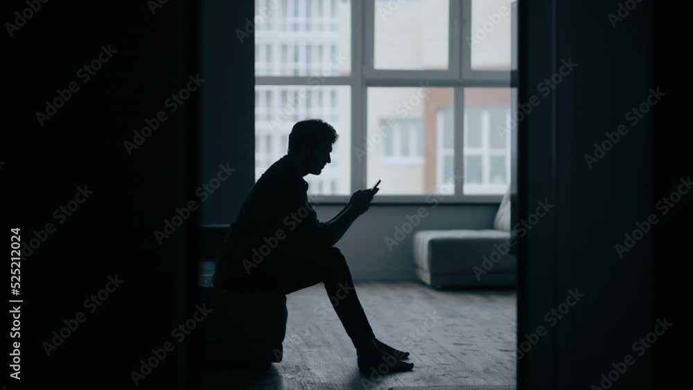 Silhouette man sitting on the sofa while get bad news from mobile phone. Depressed and hopeless male being alone with negative emotion. Mental health and economic life problem concept Silhouette man sitting on the sofa while get bad news from mobile phone. Depressed and hopeless male being alone with negative emotion. Mental health and economic life problem concept