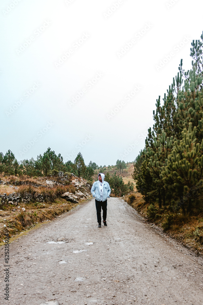 man standing in the middle of a dirt road with cloudy and cold environment