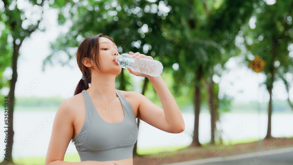 Young asian woman drinking water from a bottle while taking a break during her workout. Happy adolescence female working out in the park and taking rest a break to drink water Young asian woman drinking water from a bottle while taking a break during her workout. Happy adolescence female working out in the park and taking rest a break to drink water