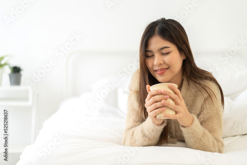 Portrait of smiling happy cheerful beauty pretty asian woman relaxing drinking and looking at cup of hot coffee or tea.Girl felling enjoy having breakfast in holiday morning vacation on bed at home