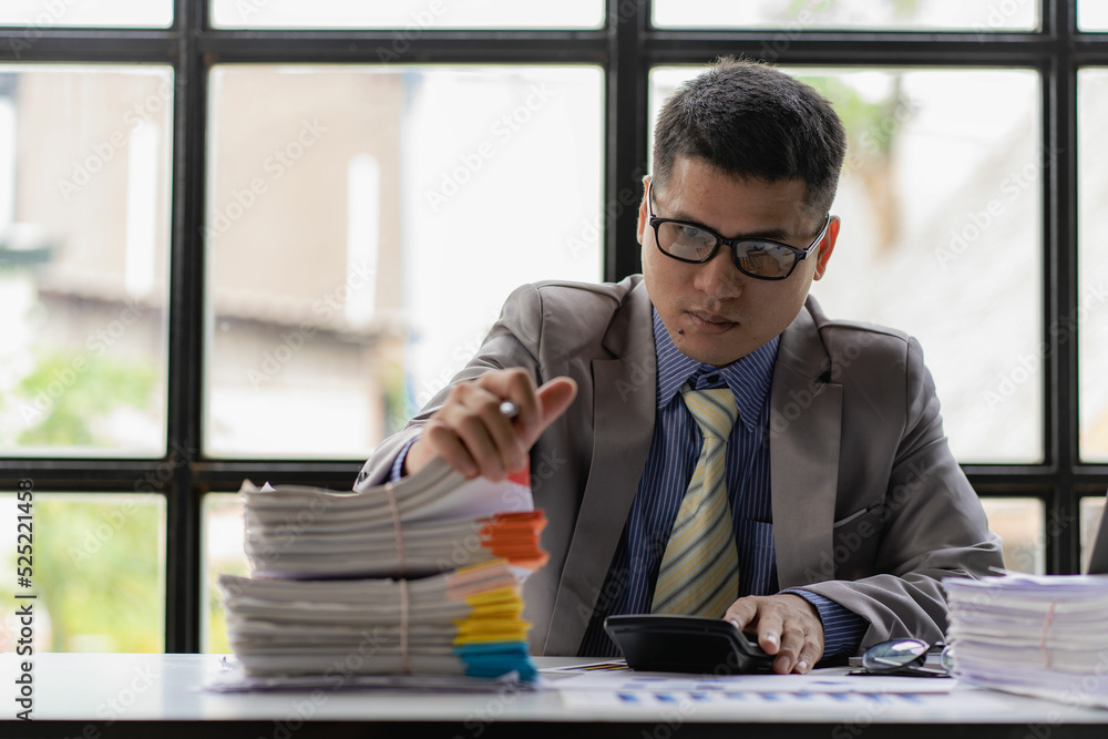 Businessman working piles of paper files to search for information on his desk at home ready. computer keyboard Work in piles of paperwork and unfinished paperwork Businessman working piles of paper files to search for information on his desk at home ready. computer keyboard Work in piles of paperwork and unfinished paperwork